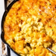 Mac and cheese in a skillet with a spoon next to a glass of wine