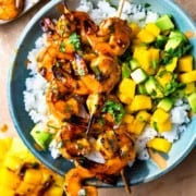 chipotle honey butter shrimp skewers served over a bowl of rice with mango avocado salsa