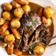 venison roast pulled apart in a serving dish with carrots, potatoes and gravy