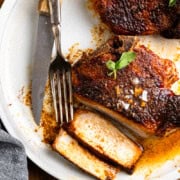 Two pork chops on a plate with a knife and fork. One pork chop is sliced.