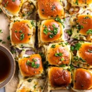 French onion roast beef sliders pulled apart on parchment paper and served with au jus