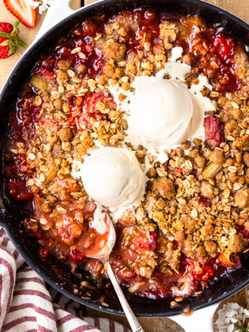 strawberry rhubarb crisp in the skillet topped with two scoops of vanilla ice cream