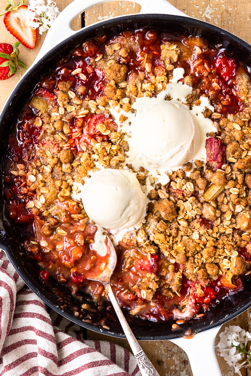 strawberry rhubarb crisp in the skillet topped with two scoops of vanilla ice cream