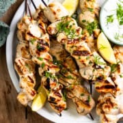 grilled chicken skewers on a plate with dip and lemon slices