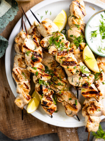 grilled chicken skewers on a plate with dip and lemon slices