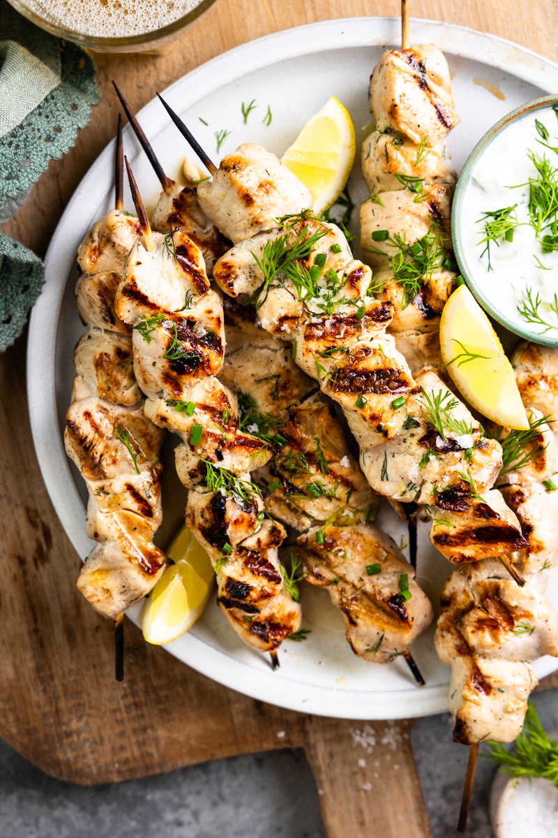 grilled chicken skewers on a plate with dip and lemon slices