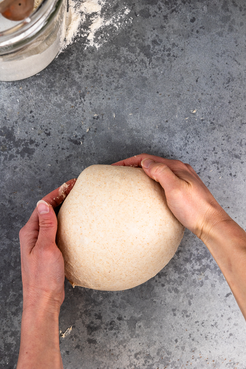 pre-shaping the dough on the counter by pushing and pulling the dough ball