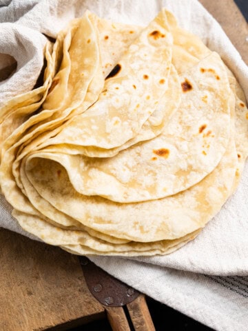 Sourdough tortillas stacked and folded in half on a towel over a cutting board.